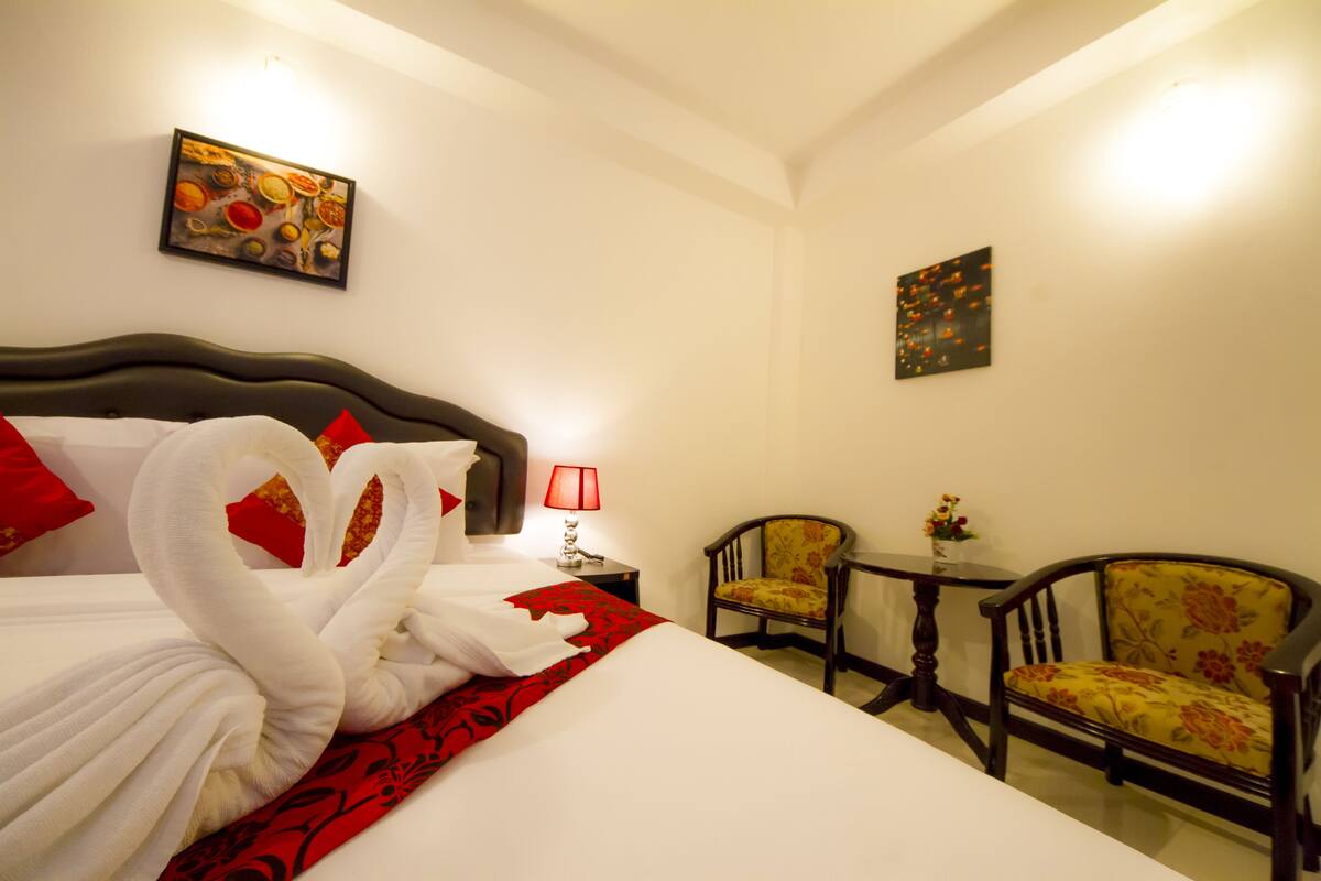 Une chambre d’hôtel avec un lit bien fait, deux chaises, une petite table et des œuvres d’art accrochées aux murs.