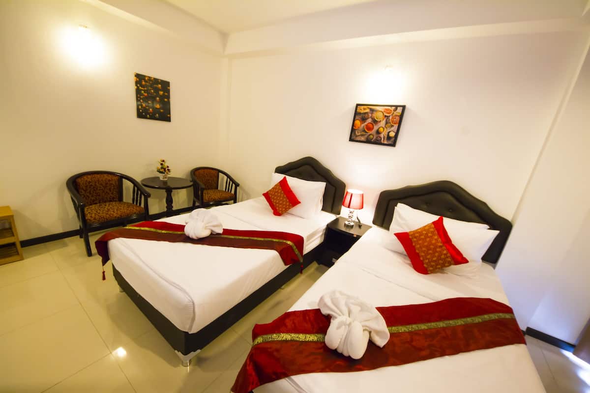 Une chambre d’hôtel avec deux lits, chacun agrémenté de draps blancs et de touches de couleur rouge, une petite table avec une lampe et deux chaises.