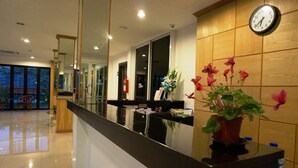A hotel reception area with a reception desk, a clock, and a potted plant. - TH Beach Hotel (Hua Hin)