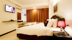 A hotel room with a bed, a TV, a desk with a lamp, and a window with curtains. - TH Beach Hotel (Hua Hin)