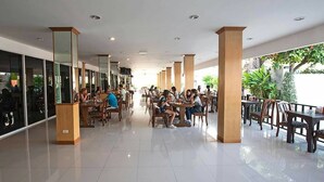 A spacious indoor dining area with multiple tables and chairs, large windows on one side, and a balcony with outdoor seating. - TH Beach Hotel (Hua Hin)