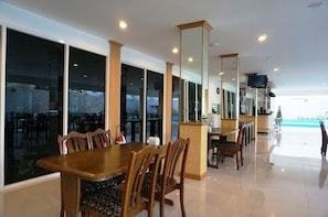 A spacious dining area with large windows, wooden tables and chairs, and a view of the sea. - TH Beach Hotel (Hua Hin)