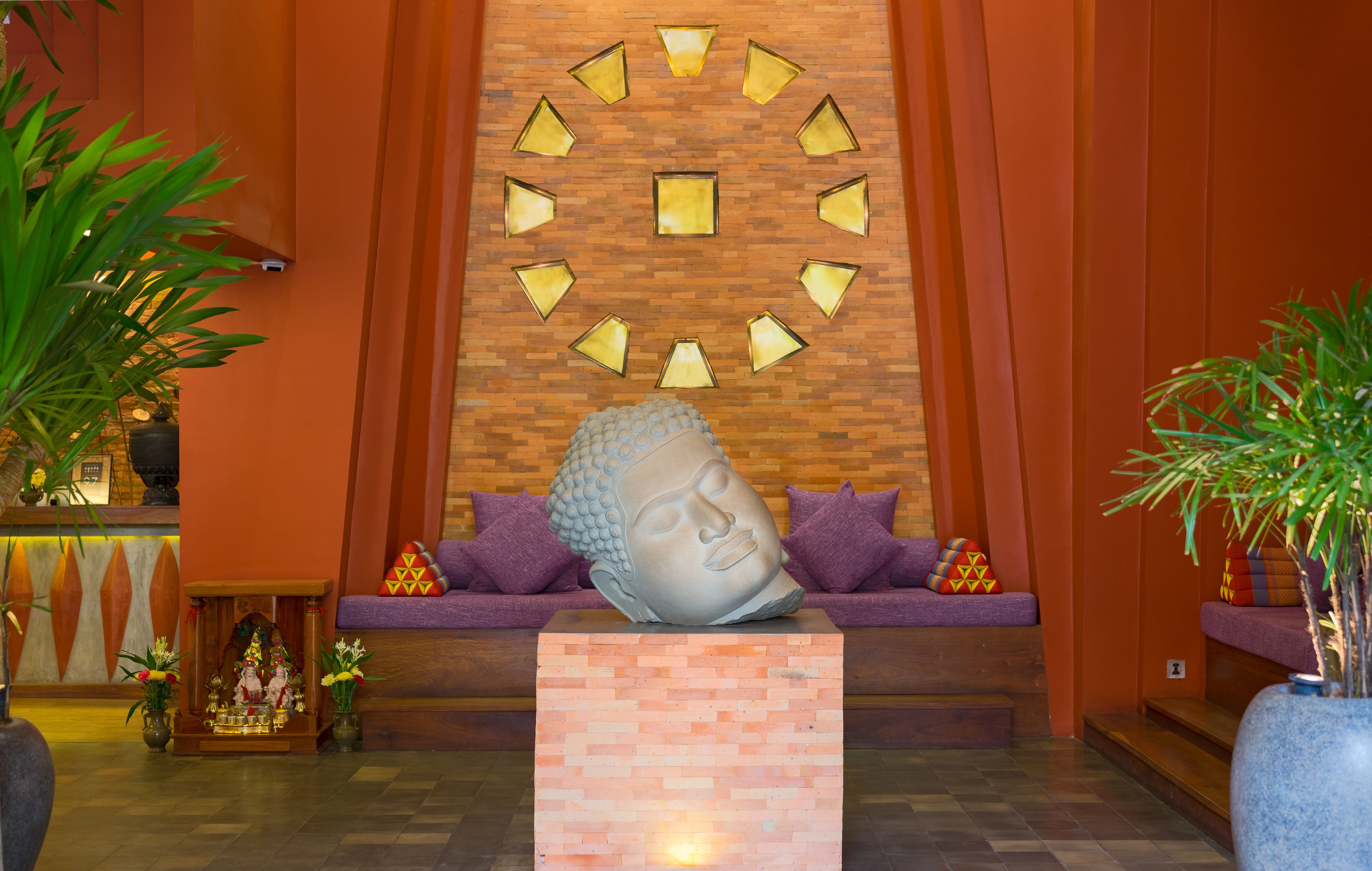 A reception area with a Buddha statue, a wooden wall with lights, and a sofa with cushions.