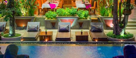 A poolside area with lounge chairs, a pool, and a restaurant with tables and chairs.
