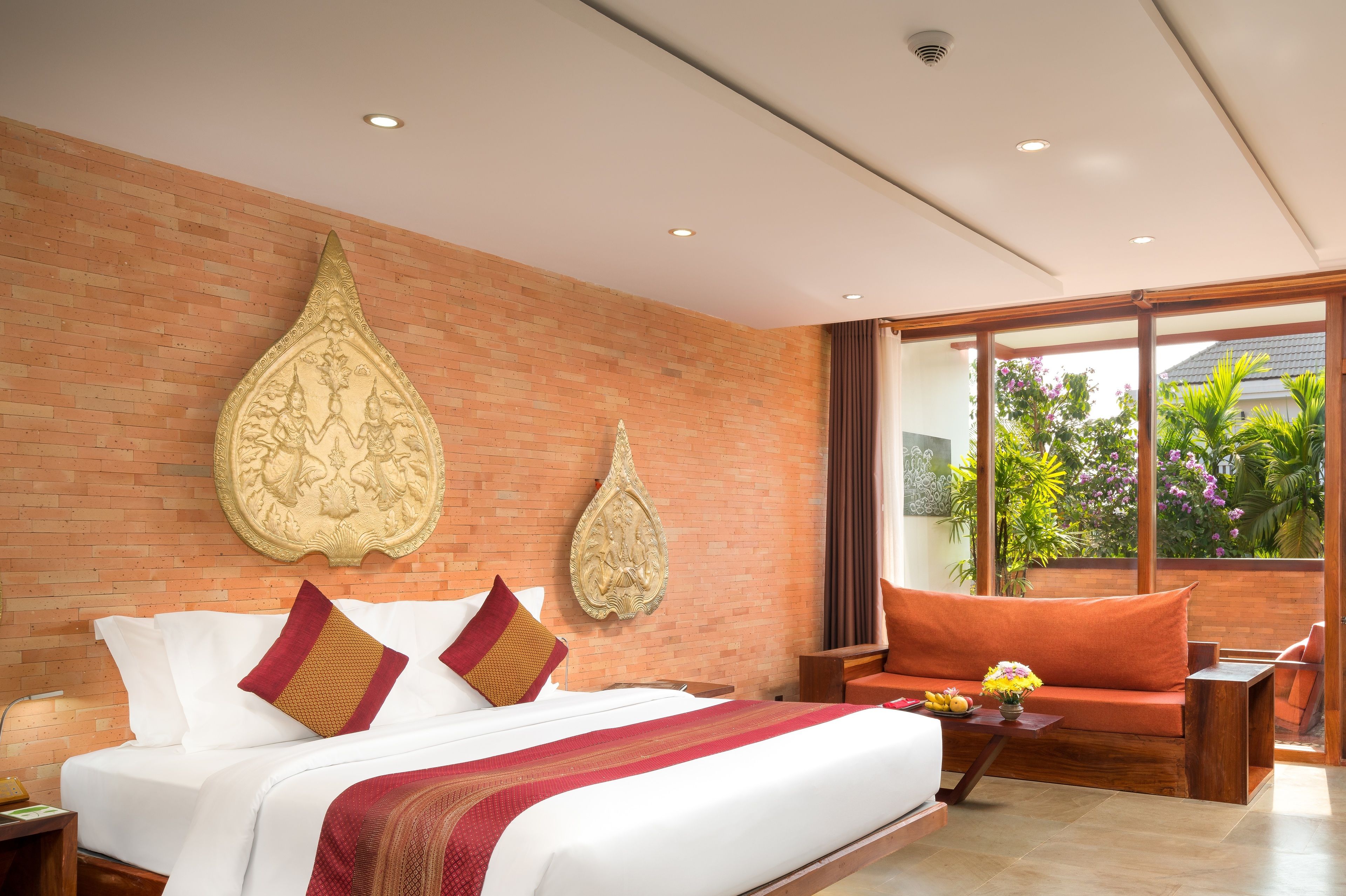 A modern hotel room with a large bed, a sofa, and a view of greenery through the window.