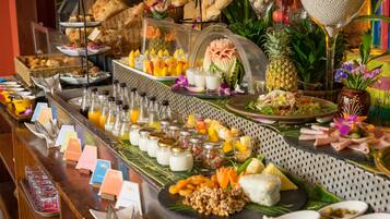 Un bufé con diversos alimentos y bebidas, que incluye frutas, pasteles y una decoración central.