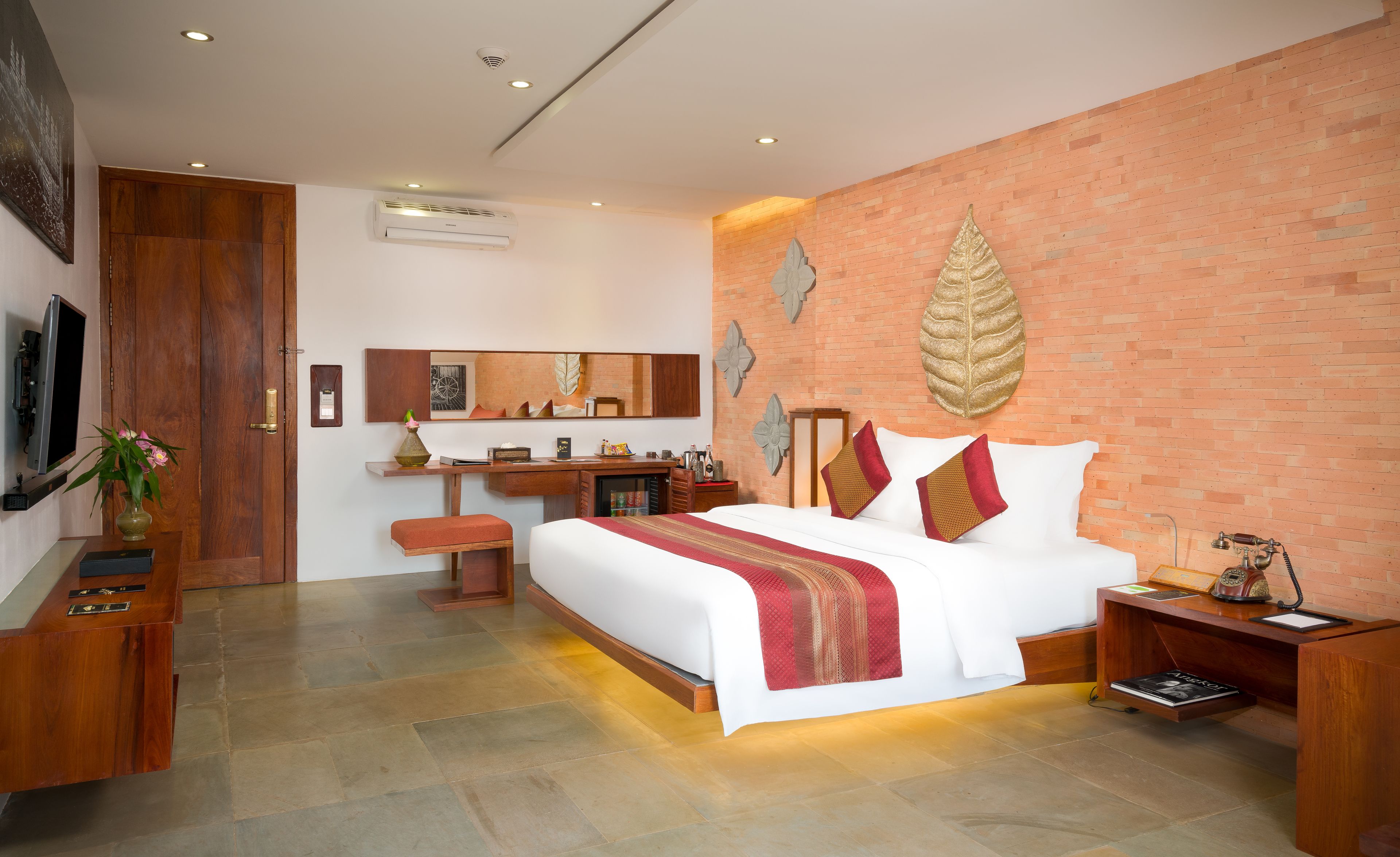 A modern hotel room with a large bed, a desk, a vanity, and a brick accent wall.