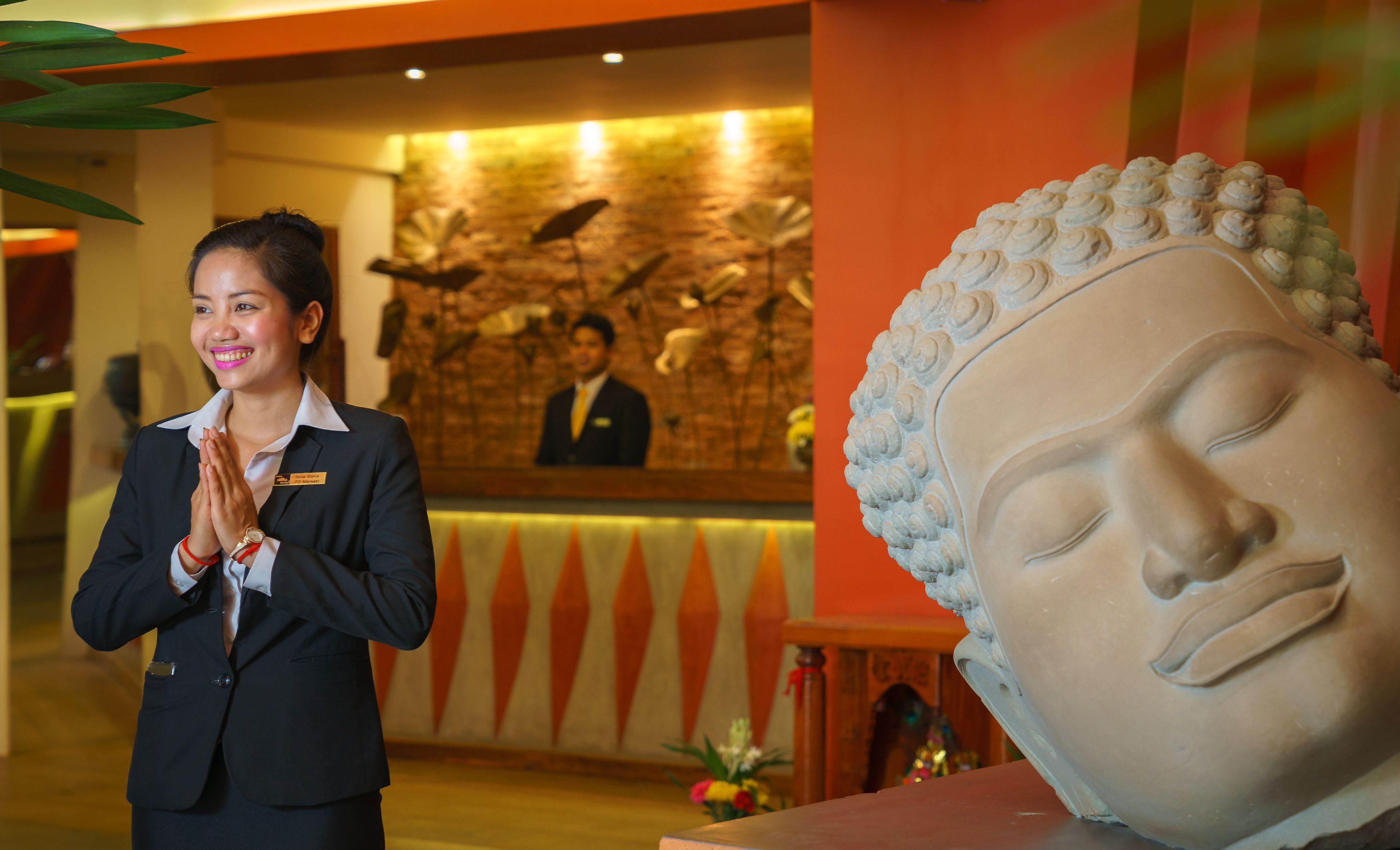 A reception area with a receptionist, a Buddha statue, and a wall with a mural.