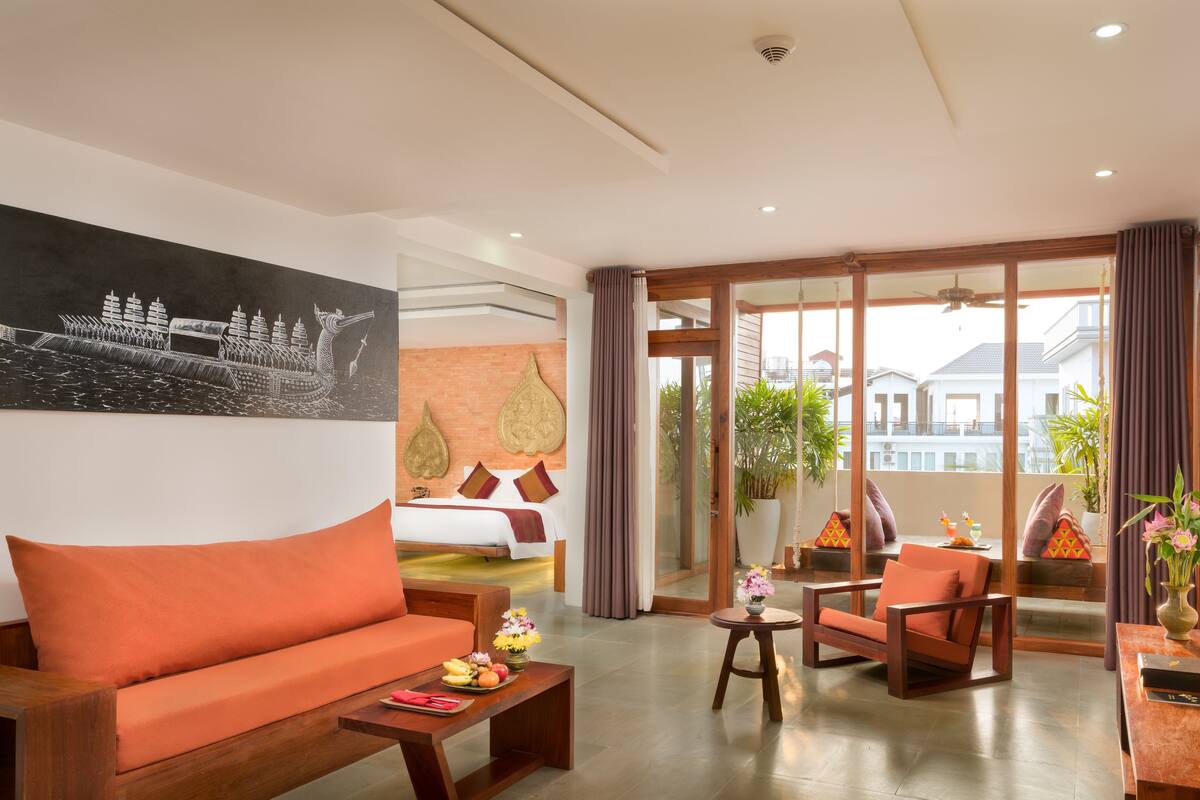 A hotel room with a bed, orange sofa, wooden coffee table, and a dining area with a table and chairs.