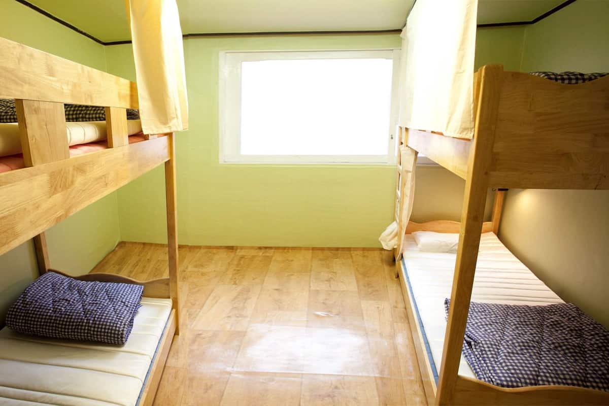A dormitory room with bunk beds, a window, and a tiled floor.