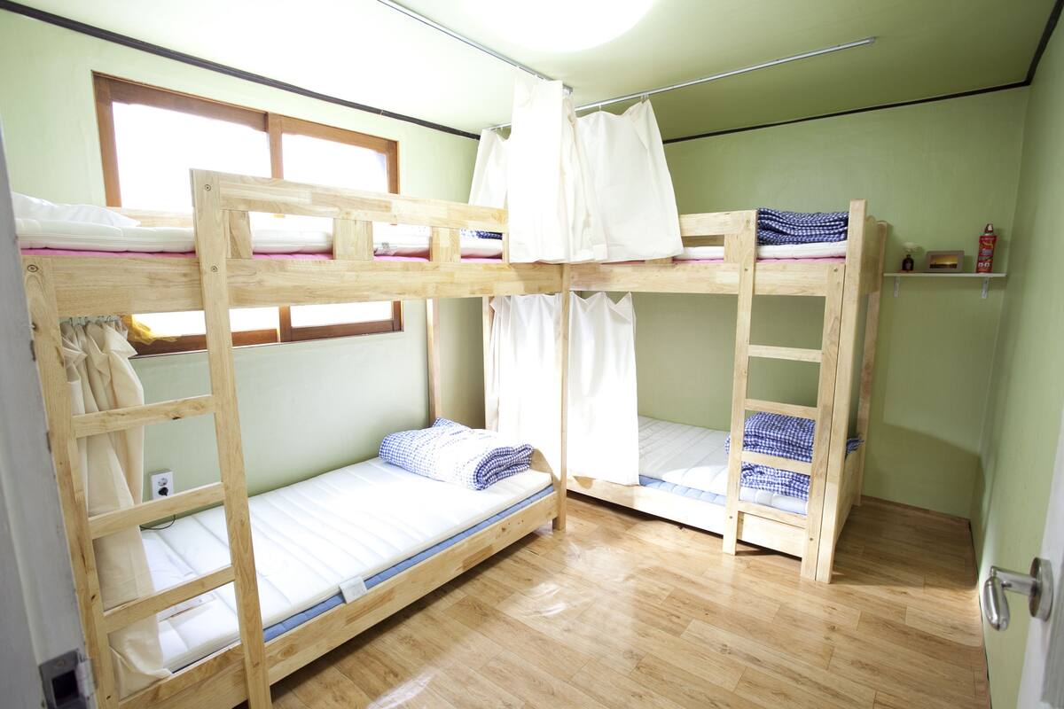 A bunk bed room with a window, wooden flooring, and a door.