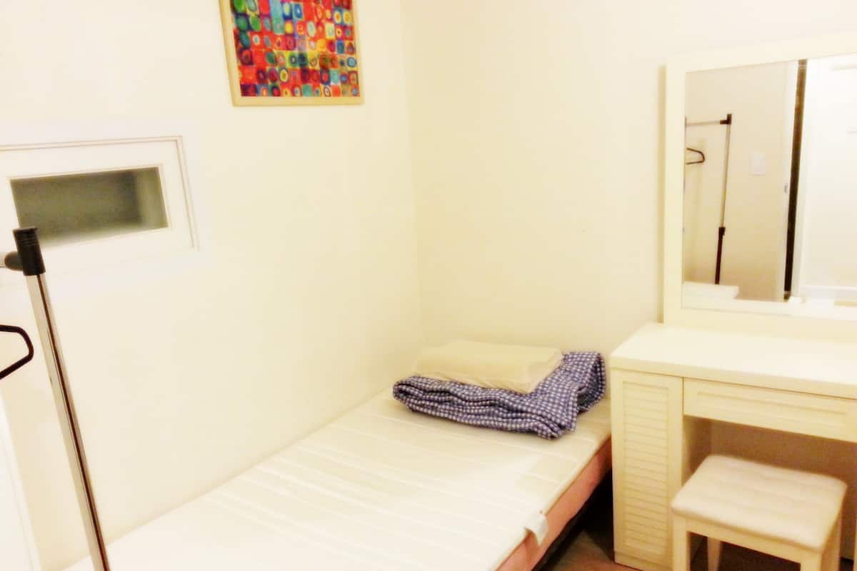 A small, single-bed room with a desk and a mirror.