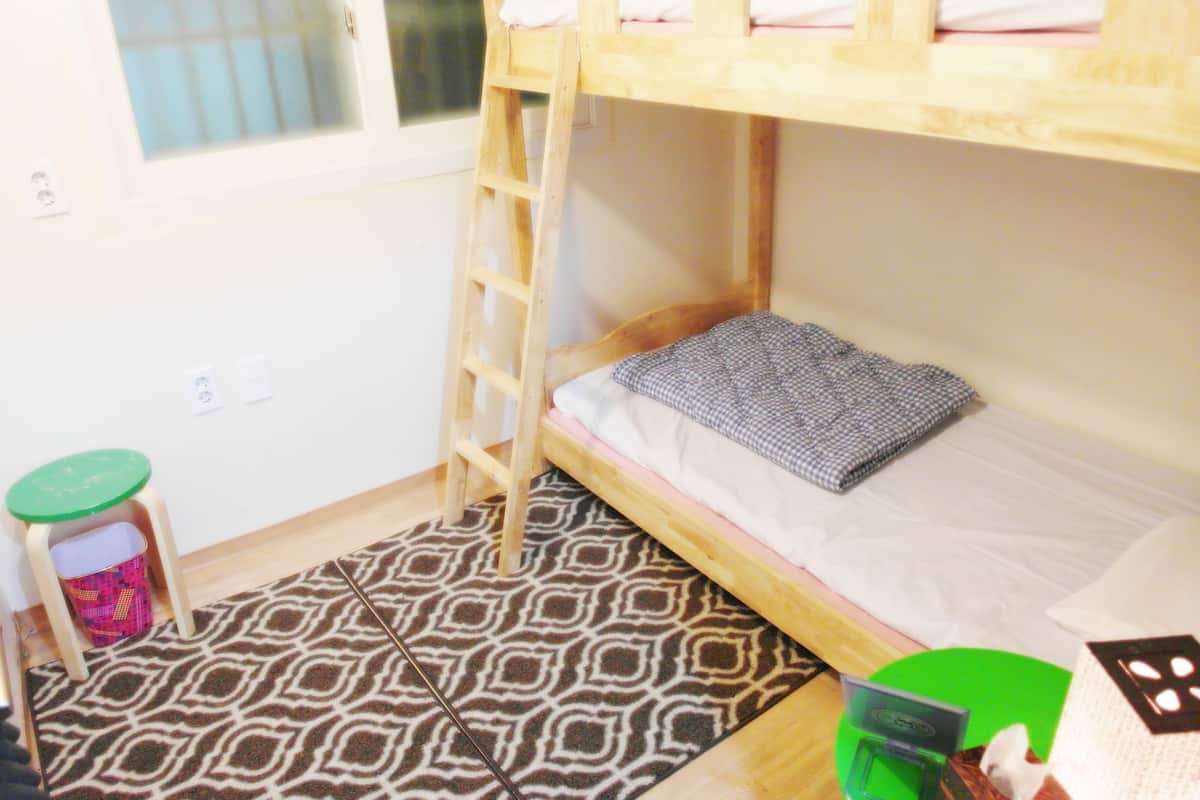 A bunk bed with a ladder, a patterned rug, a small stool, and a green container.