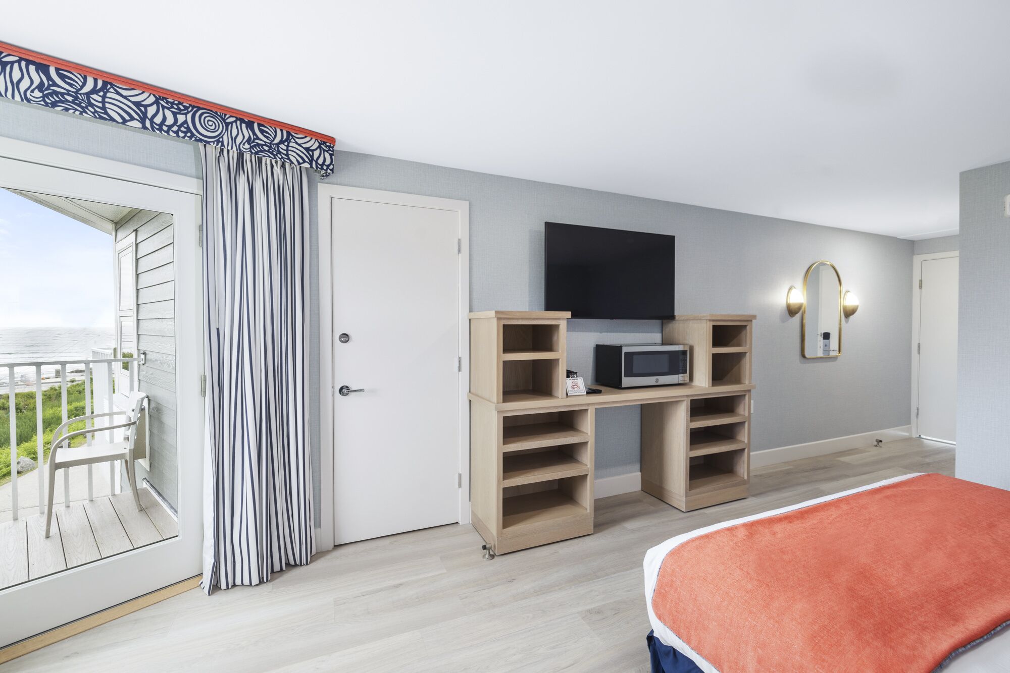 A hotel room with a balcony, a TV, a microwave, and a bed.