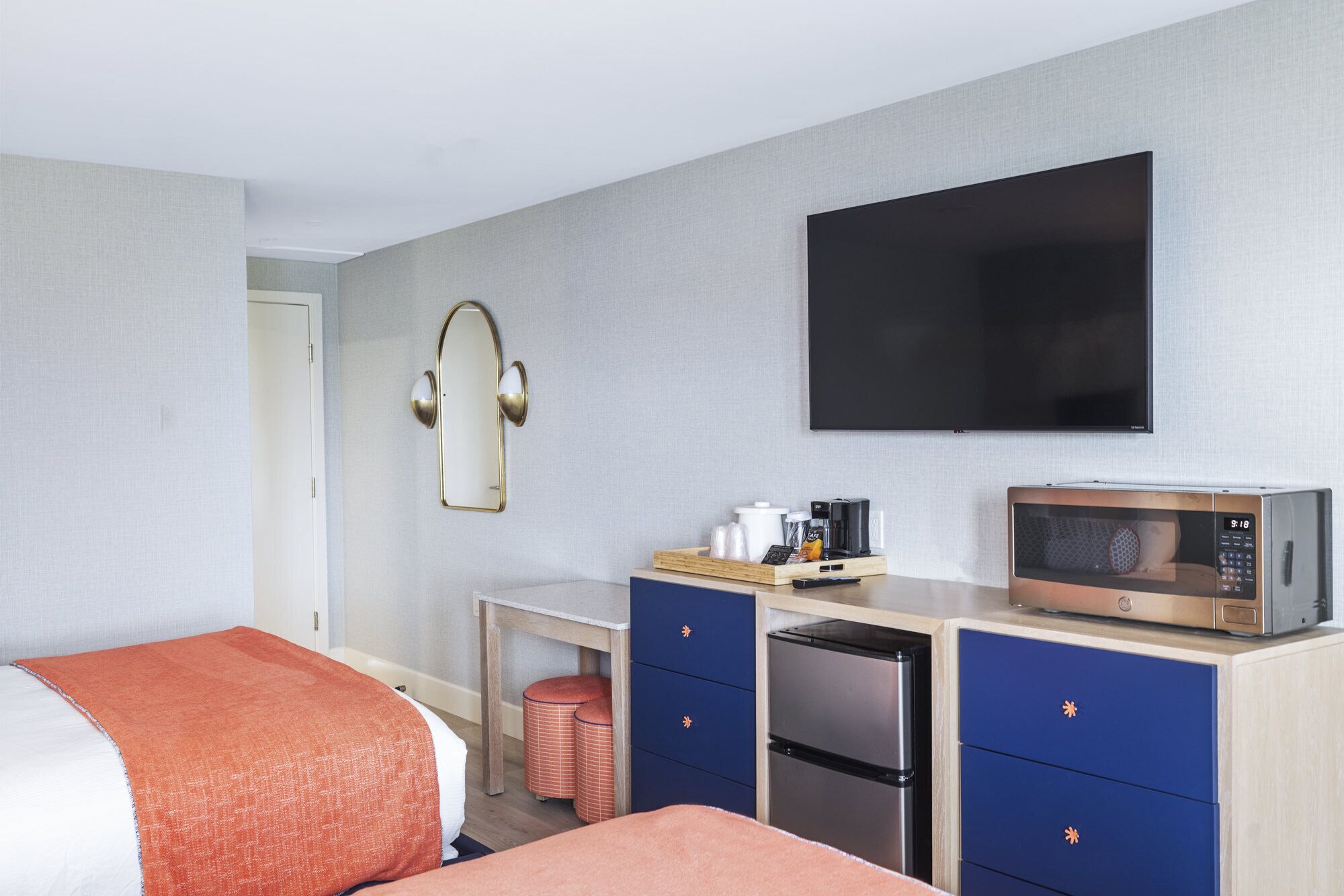 A hotel room with a bed, a desk with a microwave, a refrigerator, a television, and a small trash bin.