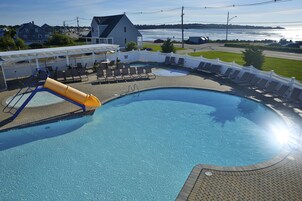 Uma piscina com escorregador, espreguiçadeiras e vista para um corpo de água.