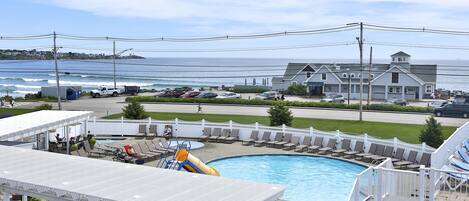 A pool area with a view of the ocean, lounge chairs, and a water slide.