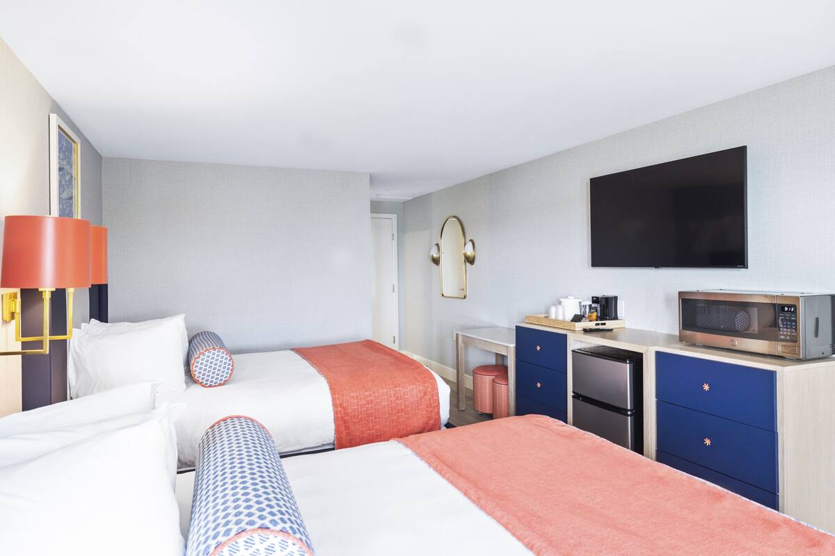 A hotel room with two beds, a desk with a microwave, a TV, and a mirror.