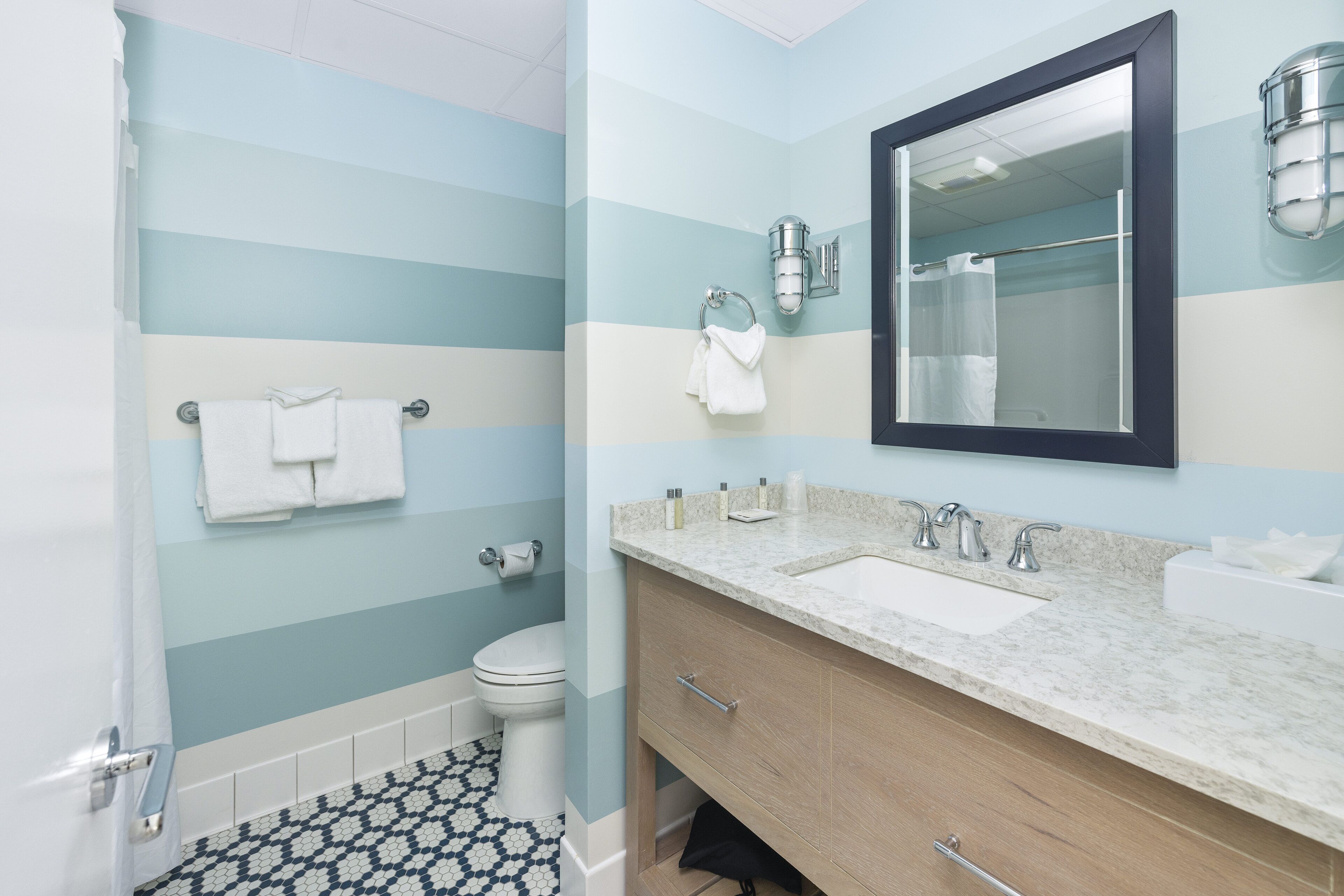 A bathroom with a striped wall design, a toilet, a sink, and a mirror.