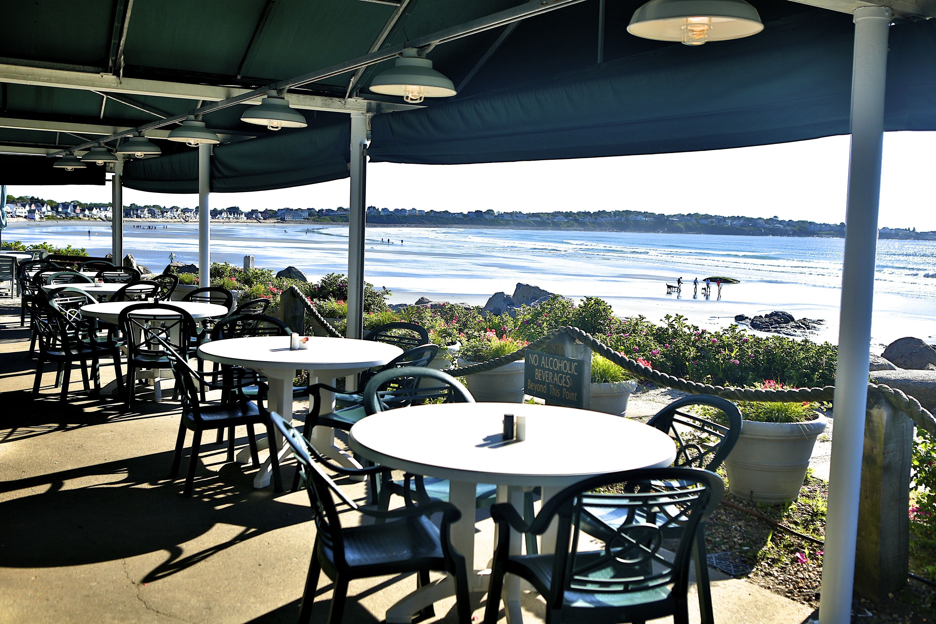 An outdoor seating area with tables and chairs, overlooking a body of water.