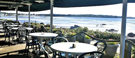 An outdoor seating area with tables and chairs, overlooking a body of water.