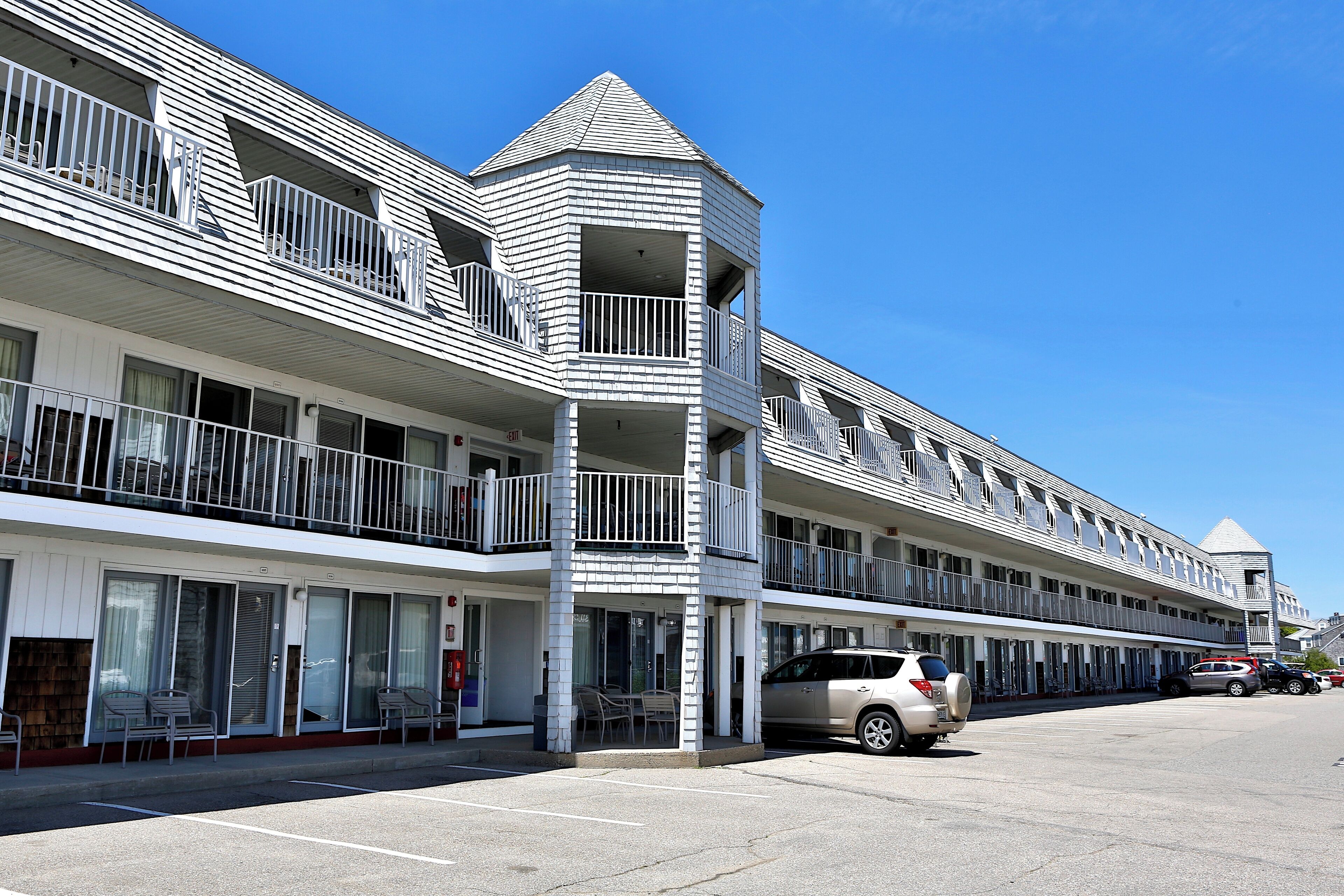 A multi-story hotel with balconies, a parking lot, and a clear blue sky.