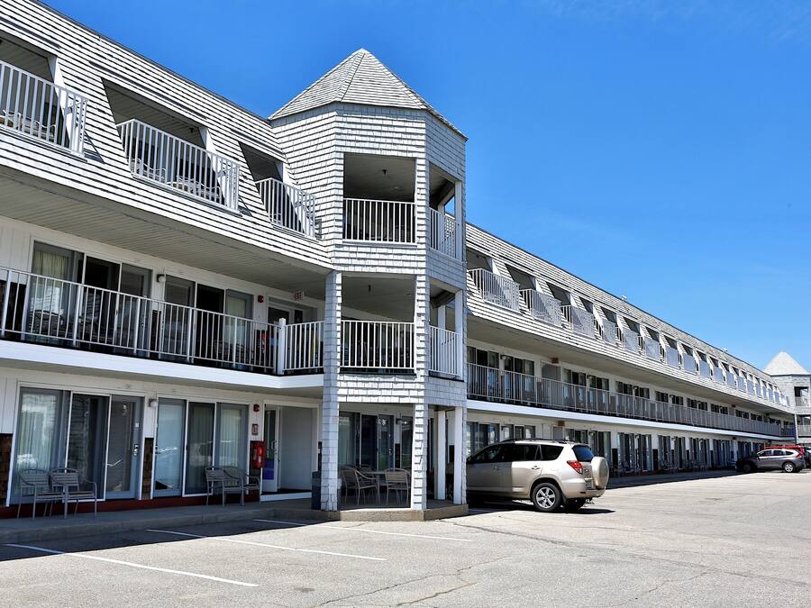 A multi-story hotel with balconies, a parking lot, and a clear blue sky.
