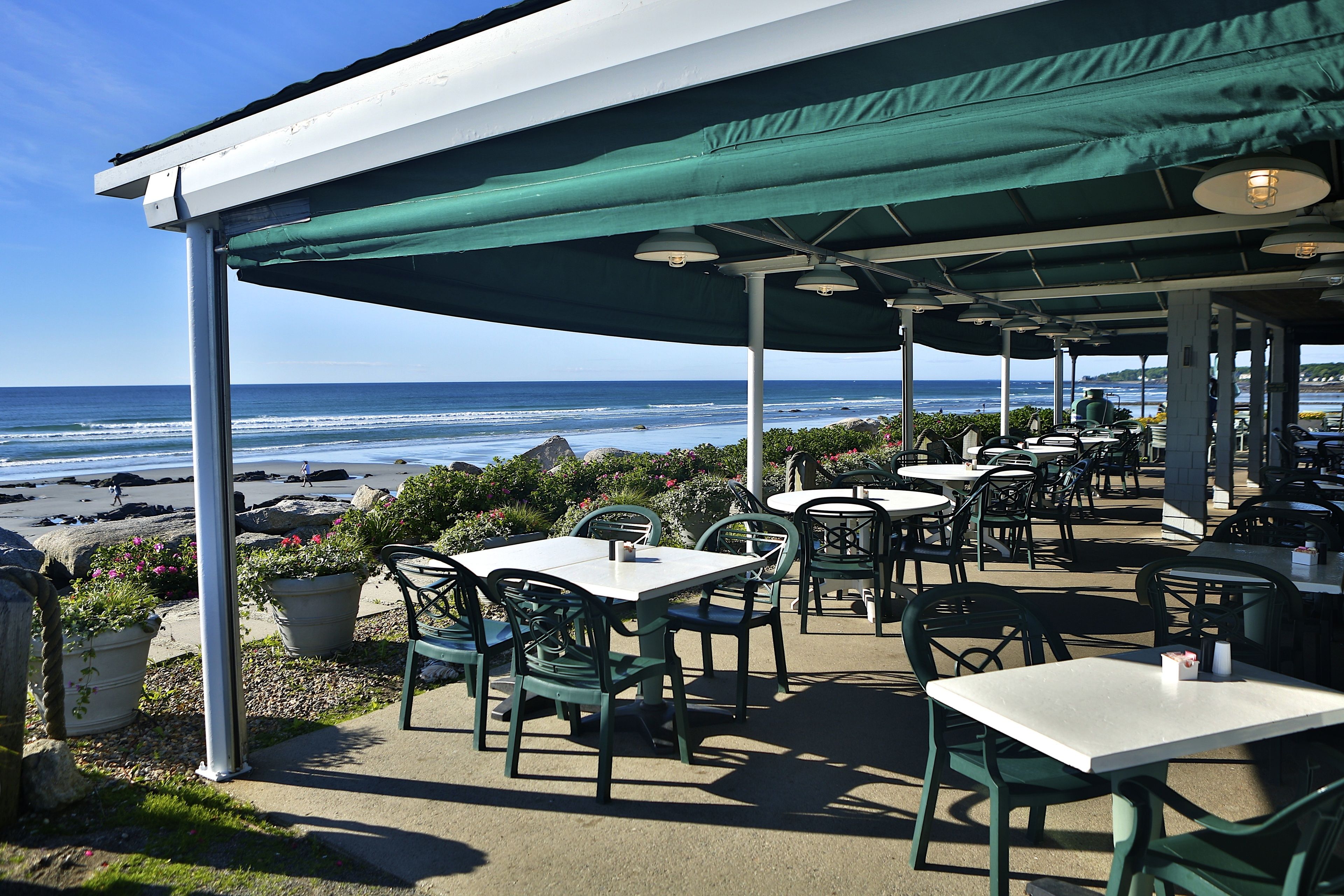 An outdoor seating area with tables and chairs, overlooking the beach and ocean.