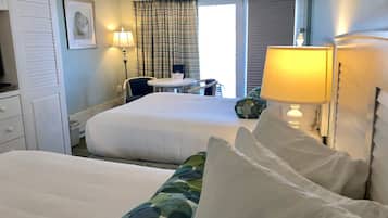 Et hotelværelse med to senge, et skrivebord, en stol og et vindue med gardiner.