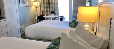Habitación de hotel con dos camas, un escritorio, una silla y una ventana con cortinas.