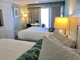 Quarto de hotel com duas camas, uma escrivaninha, uma cadeira e uma janela com cortinas.