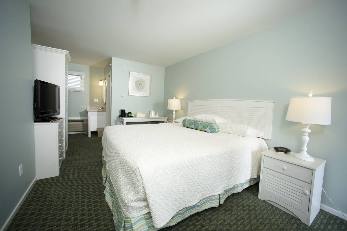 A hotel room with a bed, bedside tables, a television, and a desk with a chair.