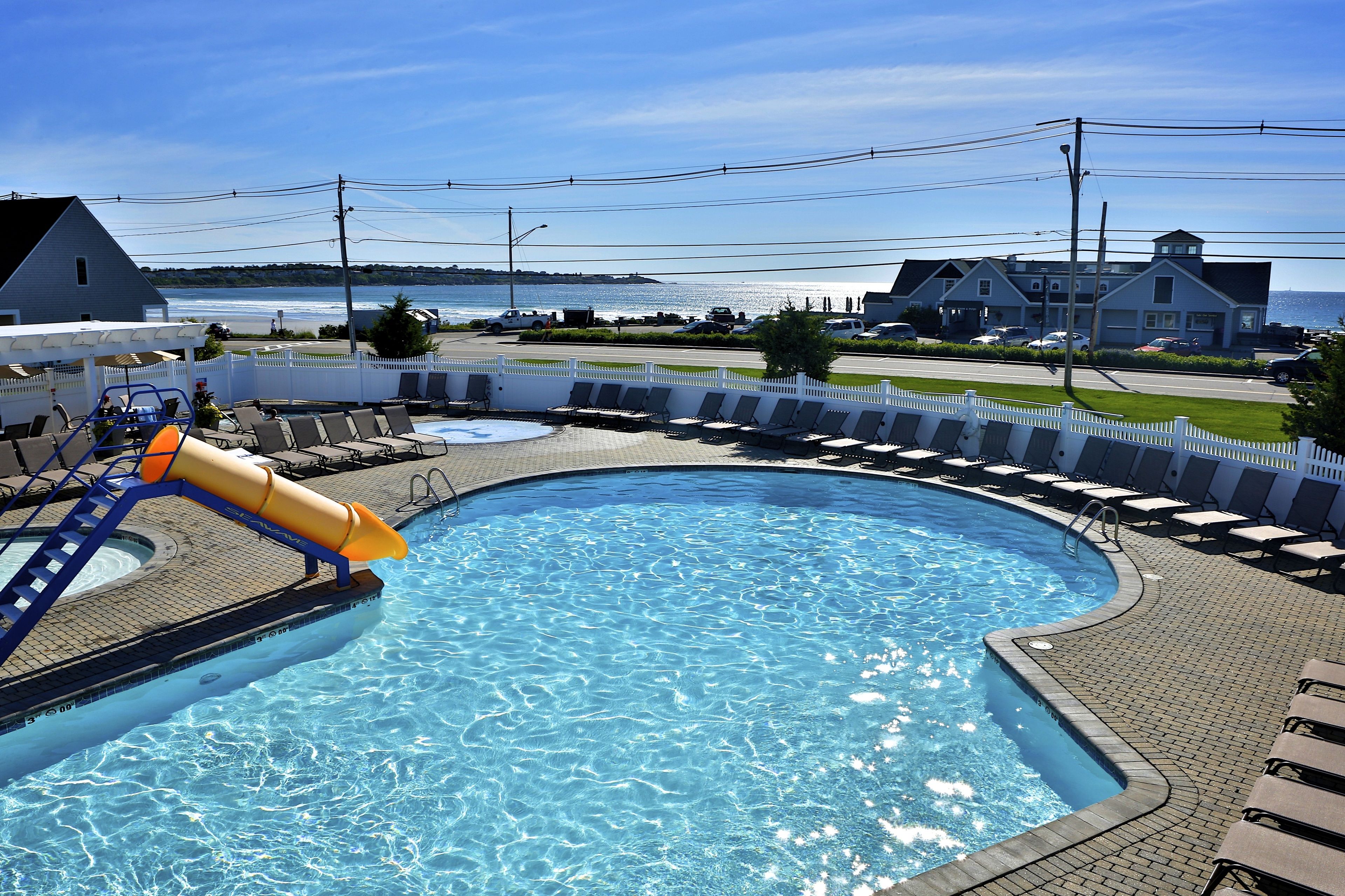 A swimming pool with a water slide, lounge chairs, and a view of the ocean and buildings in the background.