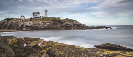 Un paisaje costero con un faro, costa rocosa y un edificio de techo rojo.