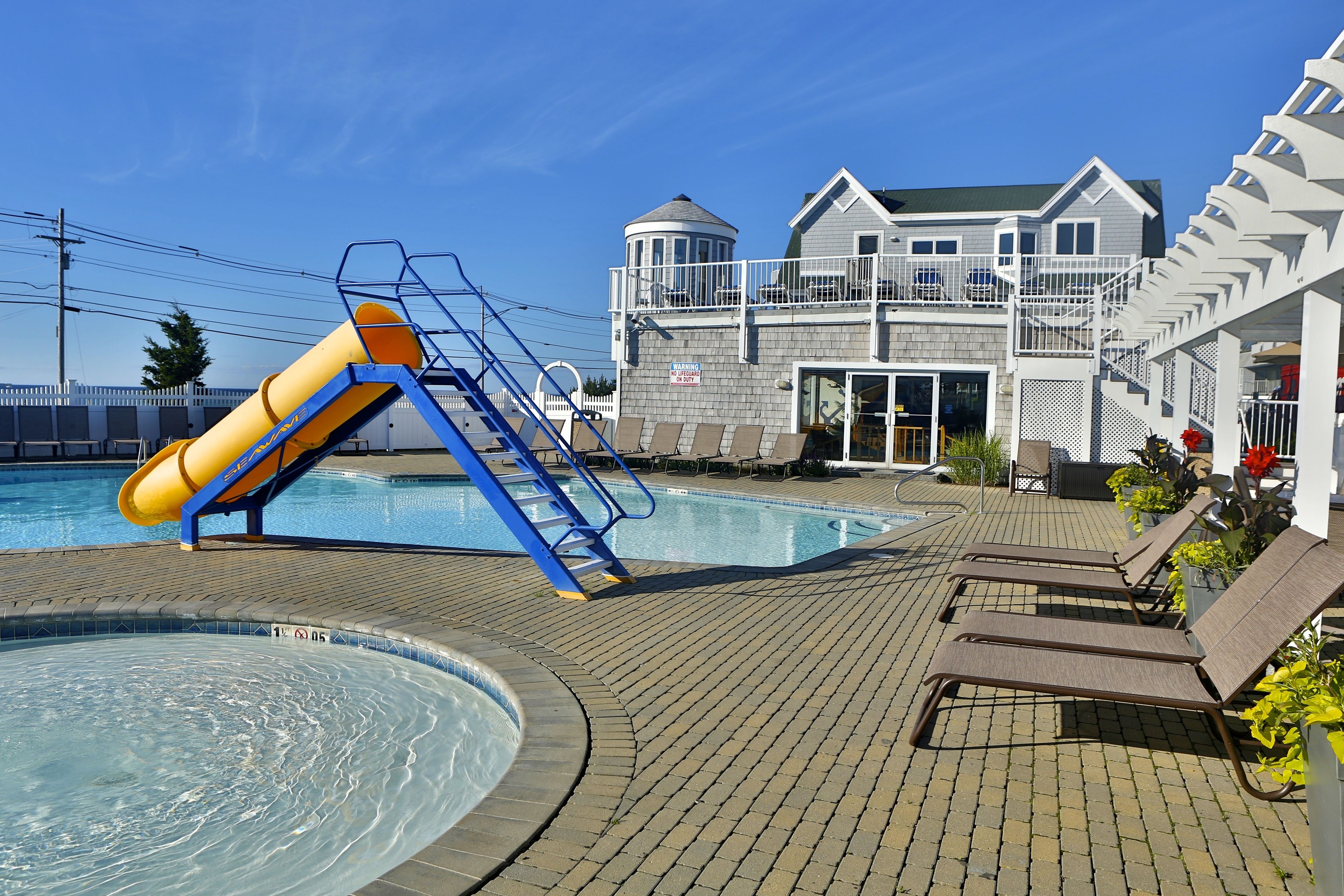 A swimming pool with a slide, lounge chairs, and a building with a balcony.