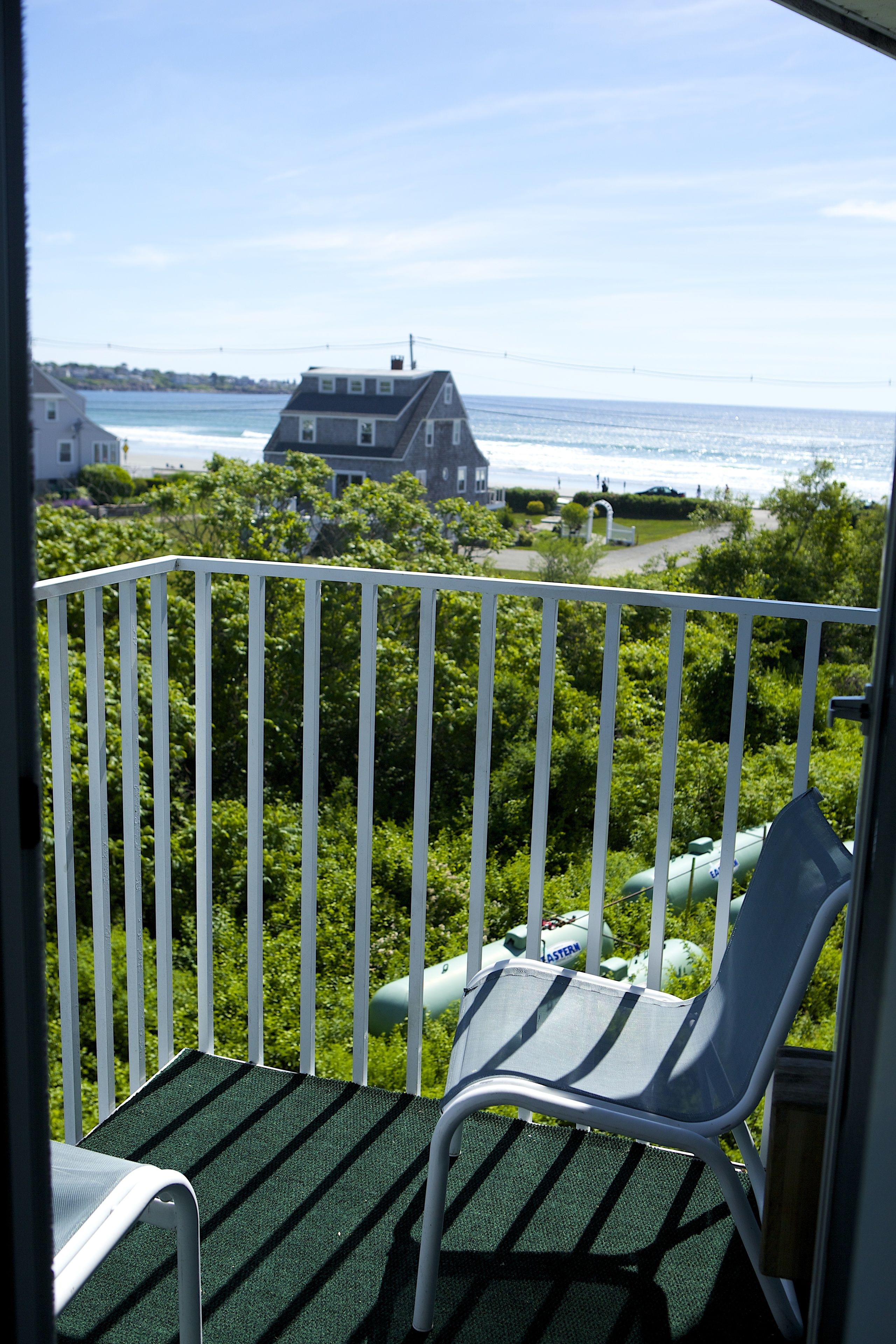 Un balcon avec vue sur l’océan et une maison en arrière-plan.