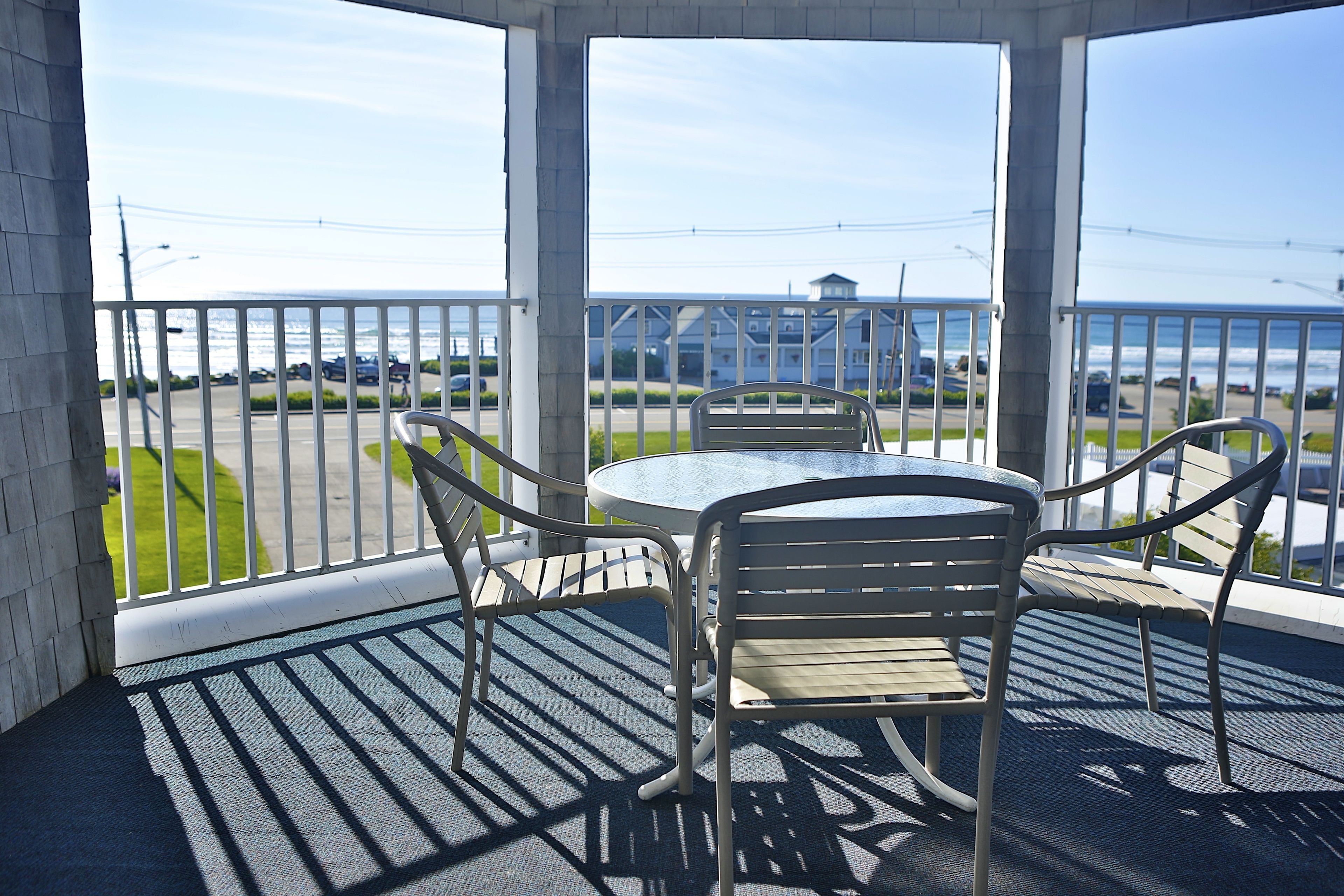 A covered outdoor seating area with a table and chairs, overlooking a parking lot and a building across the street.