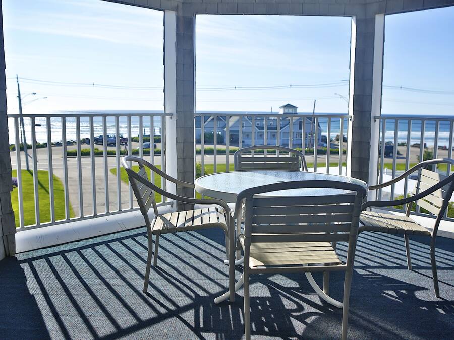 A covered outdoor seating area with a table and chairs, overlooking a parking lot and a building across the street.
