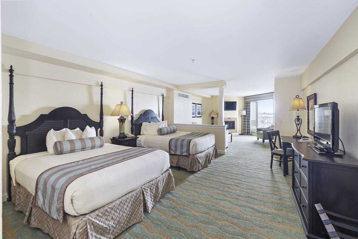 A hotel room with two beds, a desk with a TV, and a balcony with a view.