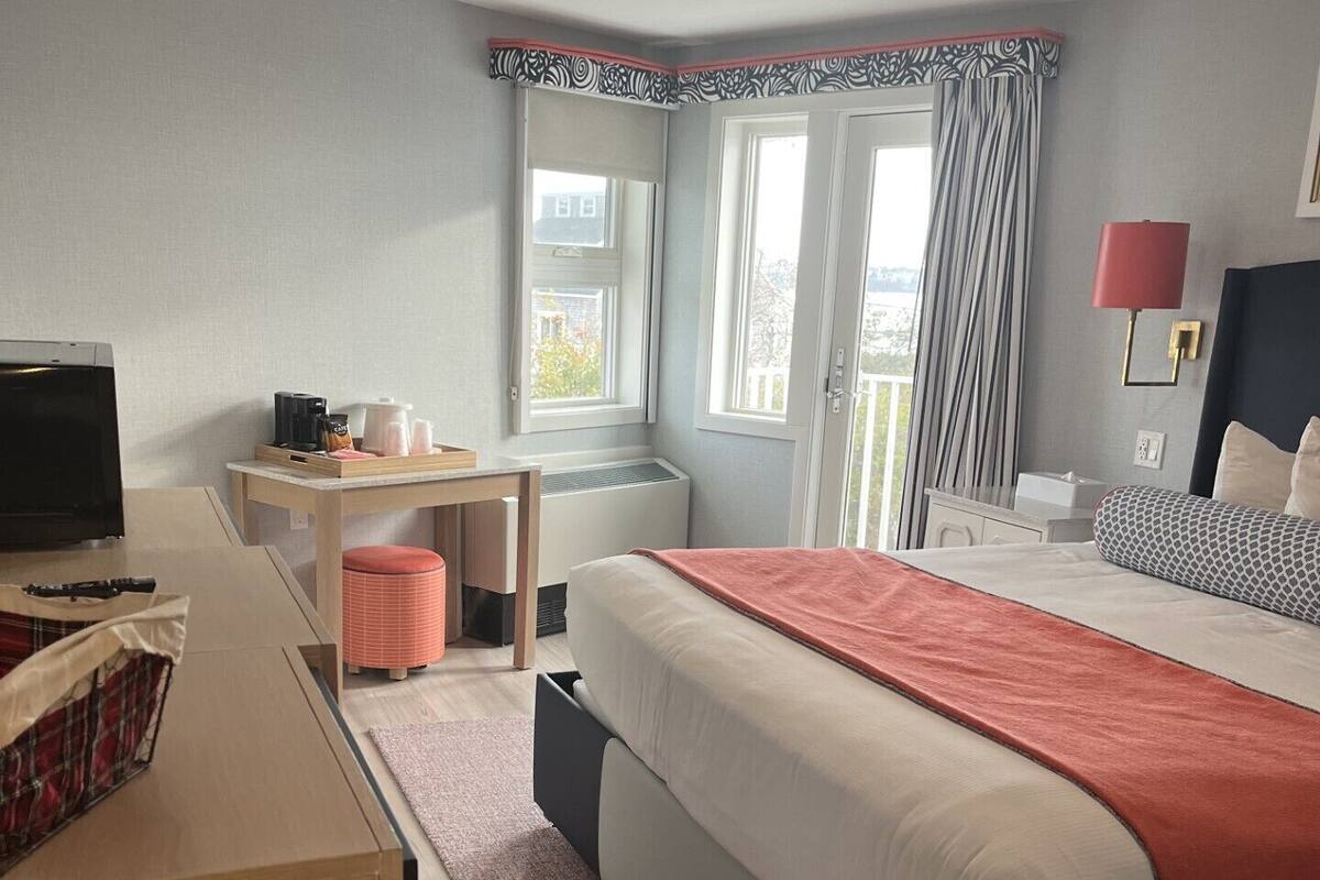 A modern hotel room with a bed, a desk, a chair, a television, and a window with curtains.