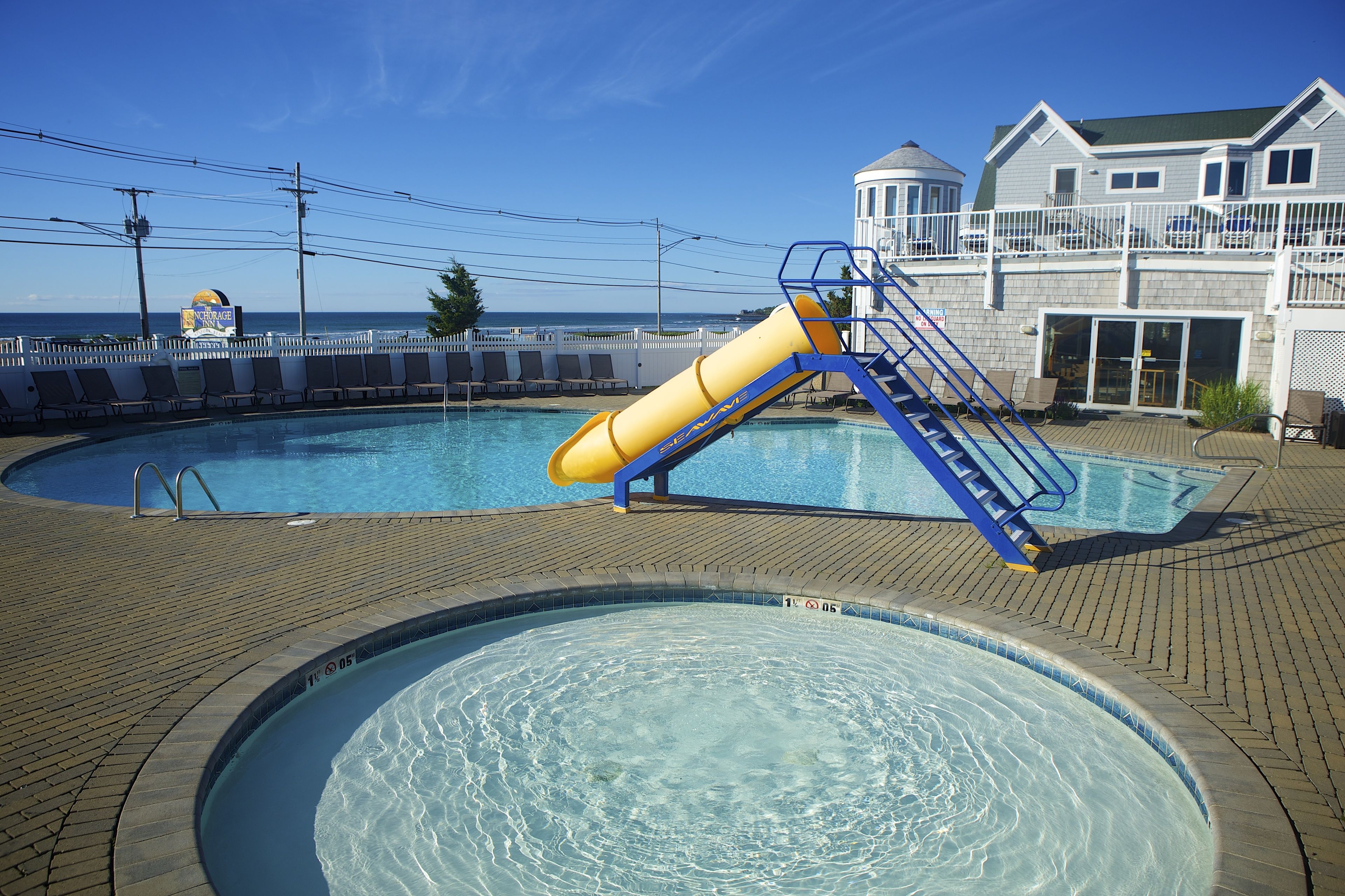A pool with a slide, a lifeguard tower, and a building with a balcony.