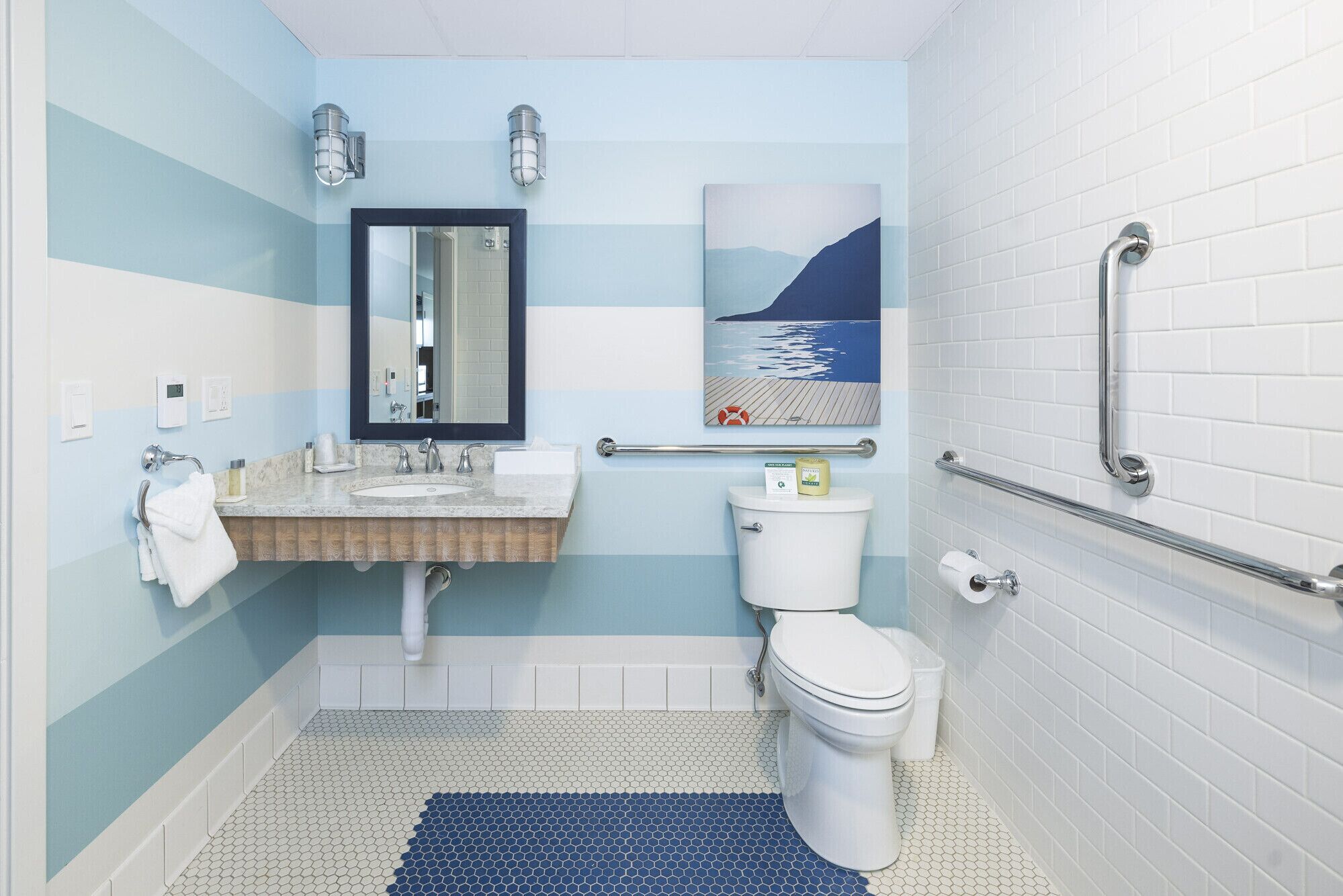 A bathroom with a sink, mirror, toilet, and a handrail.