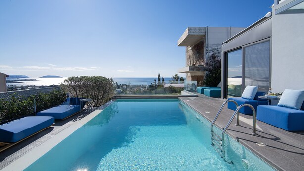 Uma piscina no terraço com águas cristalinas azuis, cadeiras de descanso azuis e vista para o mar.