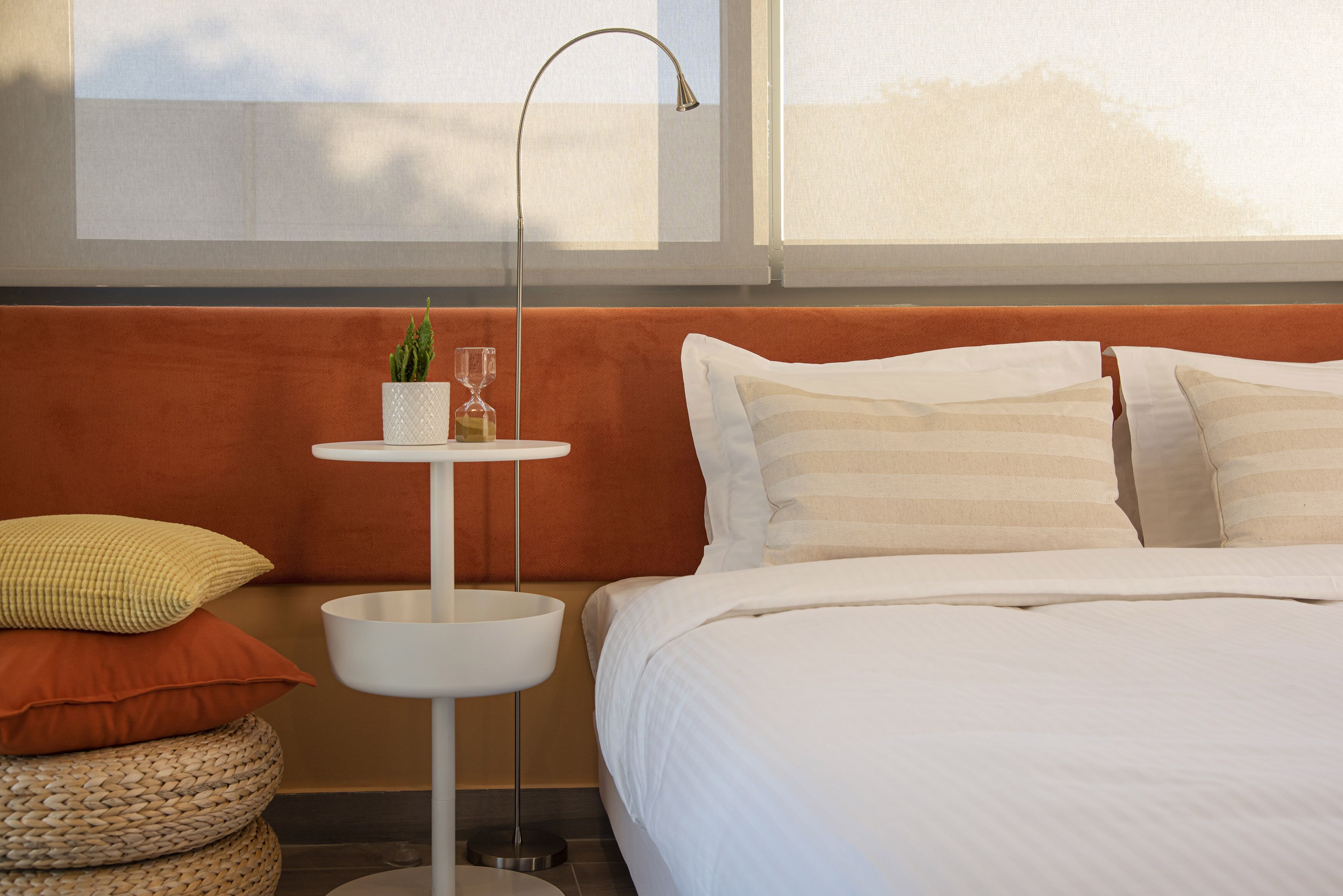 A neatly arranged hotel room with a bed, pillows, a bedside table with a plant and a glass, and a window with a view.