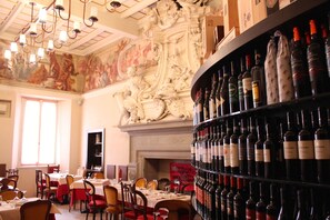 A restaurant with ornate ceiling artwork, a wine rack with various bottles, and tables set for dining. - Le stanze del Lago (Como)