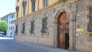 Un edificio histórico con una puerta de madera grande, fachada de piedra y ventanas con ornamentación de hierro forjado.