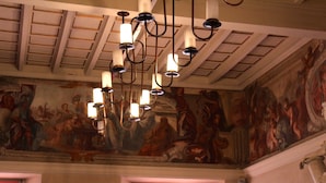 Una habitación con techo alto, un candelabro y un mural en la pared.