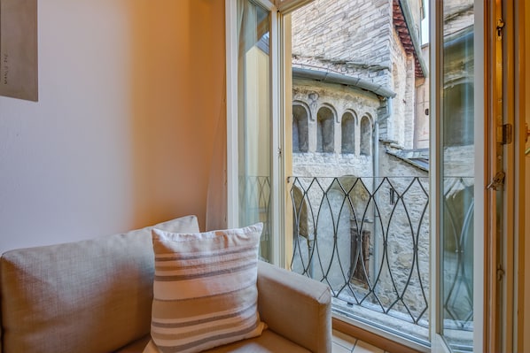 A room with a sofa and a window overlooking a stone building with arches.