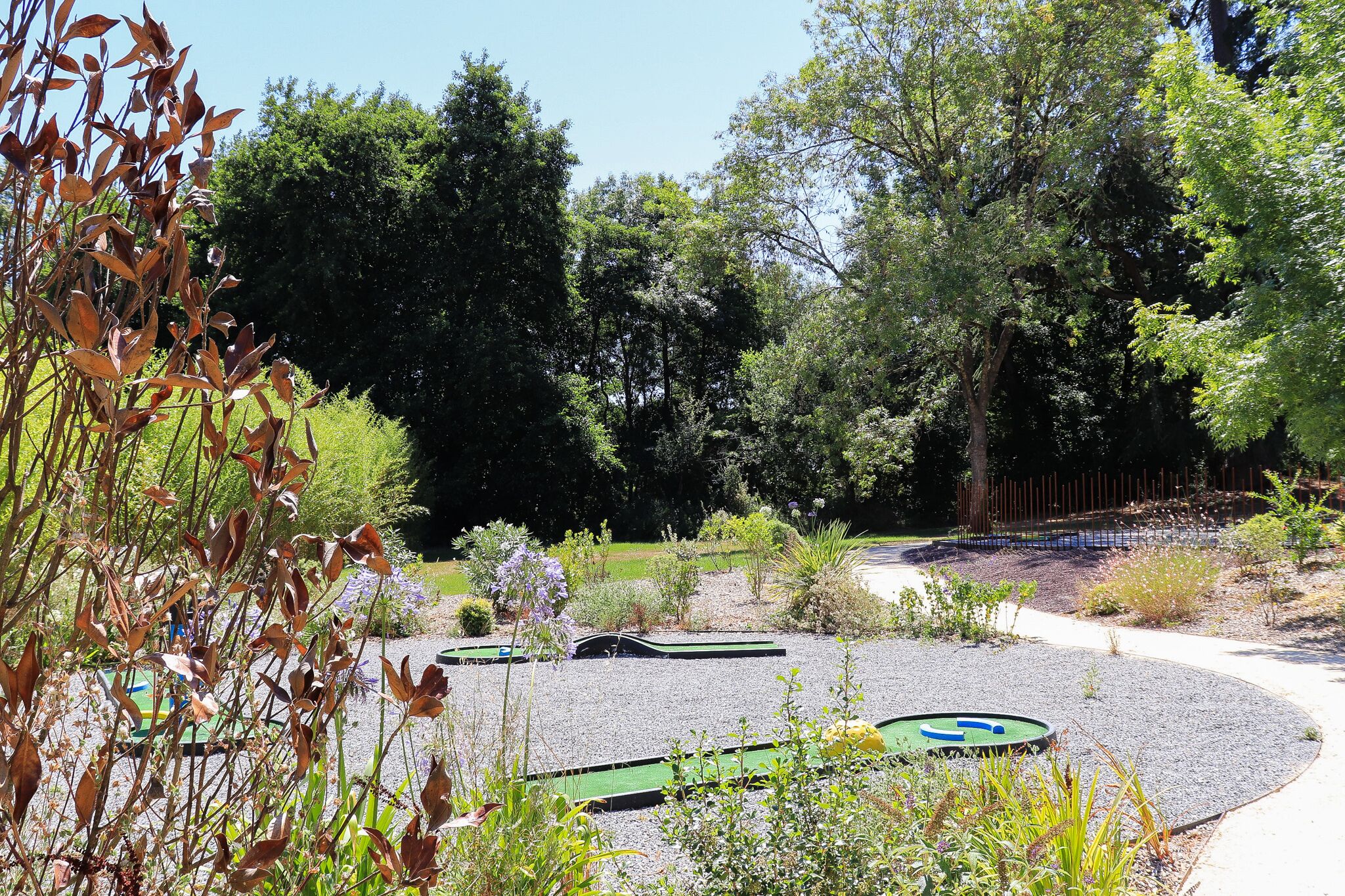 A garden with a gravel path, green play structures, and various plants.