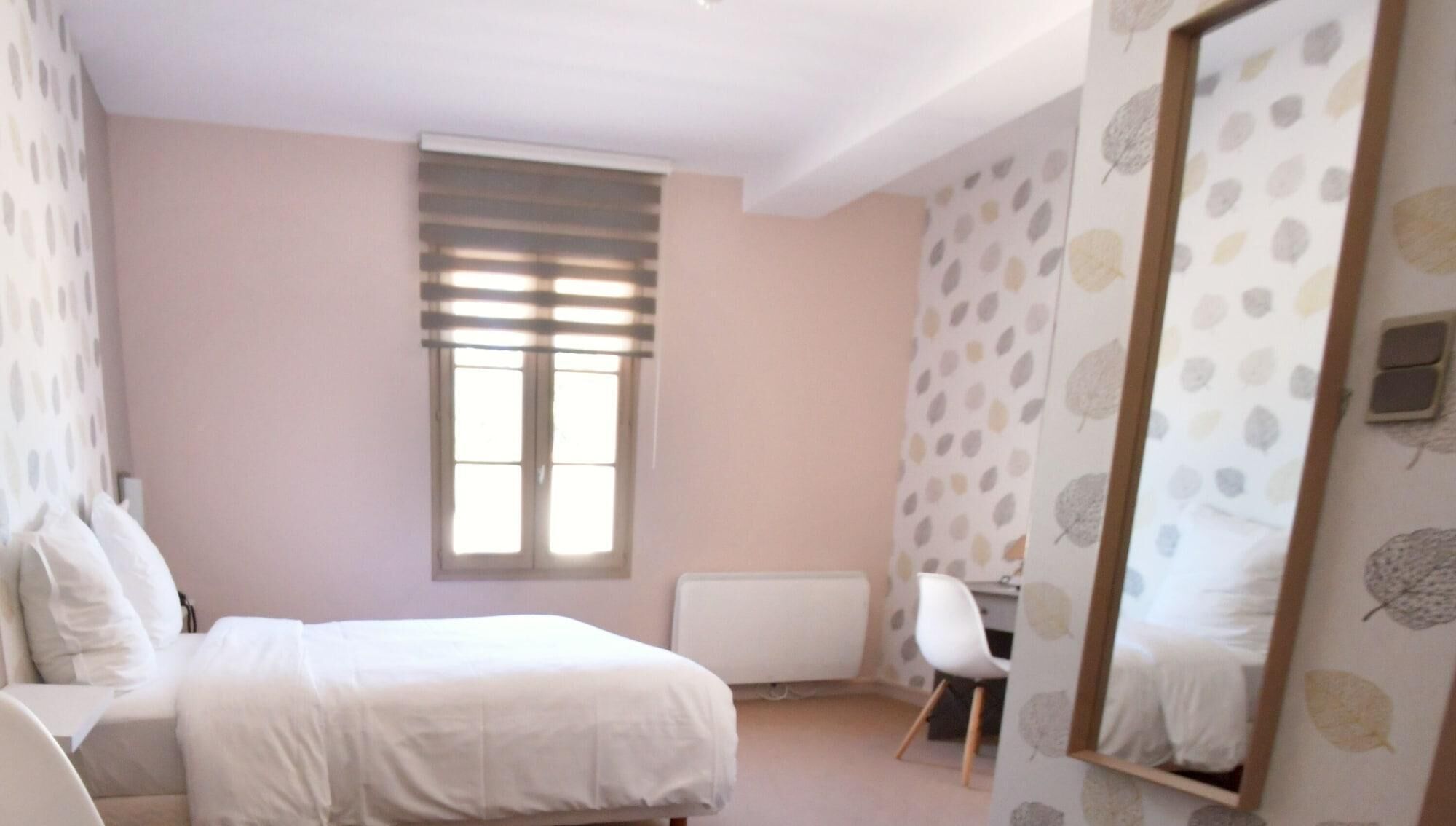 A bedroom with a bed, a desk, a chair, a window with blinds, and a mirror.